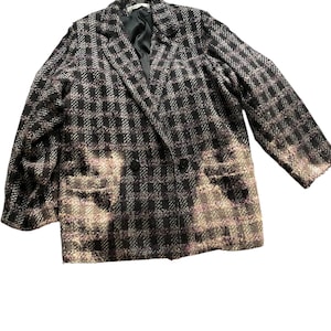 May include: A double-breasted blazer in a black and pink plaid pattern. The jacket has a notched collar, two front pockets, and a black lining. The fabric has a textured appearance, and the blazer appears to be made of a woven material.