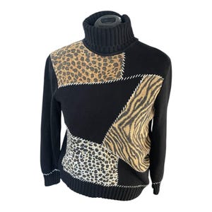 May include: Black turtleneck sweater with animal print patchwork design. The sweater features leopard, zebra, and other animal print patterns stitched onto a black base. White stitching outlines the patchwork.