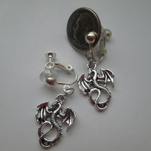May include: A pair of silver clip-on earrings with a silver dragon charm hanging from each earring.