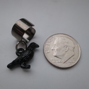 May include: A silver ear cuff with a black crow charm. The charm is about the size of a dime.