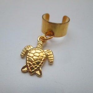 May include: Gold-colored ear cuff featuring a turtle charm. The ear cuff has a simple band design that wraps around the ear. The turtle charm is detailed with textured shell and flippers, creating a nautical theme.