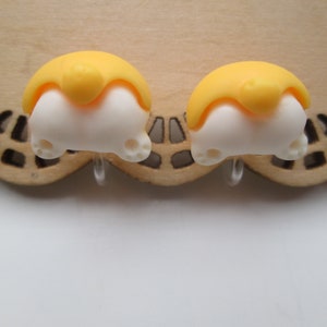May include: A pair of yellow and white cartoon dog bottom earrings. The earrings are made of polymer clay and have a cute, playful design.
