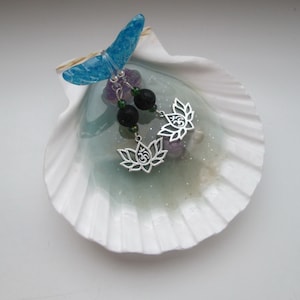 May include: A pair of silver earrings with a lotus flower design and an Om symbol. The earrings are hanging from black lava beads and green beads.