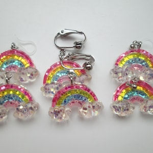 May include: A pair of rainbow and cloud earrings with a silver clip-on back. The earrings are made of clear plastic with glitter and iridescent accents.