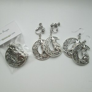 May include: A pair of silver earrings featuring a wolf howling at the moon, set in a Celtic knot design. The earrings are available in both clip-on and post styles.