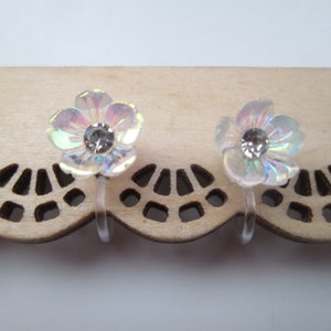 May include: A pair of iridescent white flower-shaped clip-on earrings with clear rhinestone centers.
