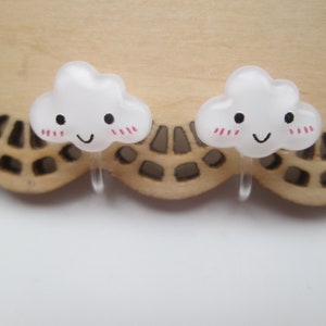 May include: A pair of white cloud-shaped earrings with pink blush and a smiling face.