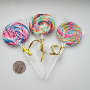 May include: Three colorful swirl lollipops wrapped in clear plastic with gold ribbon ties. The lollipops are on a white background.