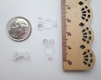 May include: Three clear plastic earring backs, one is a single piece and the other two are two-piece sets. The backs are shown next to a US dime for size comparison.