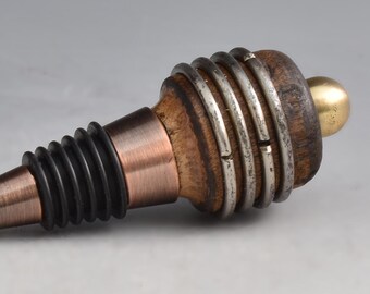 May include: A decorative wine bottle stopper with a copper-colored tip and a black rubber seal. The stopper features a wooden body with silver-colored rings and a gold-colored ball on the end. The design is elegant and suitable for wine enthusiasts.