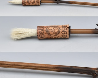 May include: A handcrafted calligraphy brush with a natural wood handle and a cork barrel. The brush features a light-colored bristle head and a loop at the end. The cork barrel has printed text and a design.