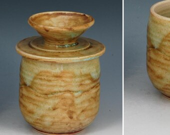 May include: A ceramic butter keeper with a mottled tan and light green glaze. The set includes a bell-shaped lid with a wide rim and a cylindrical base. Text on the image indicates dimensions of 4.7 inches in height and 3.7 inches in width.