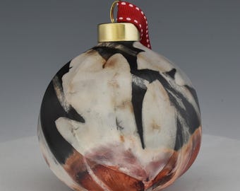 May include: A ceramic Christmas ornament with a gold cap and a red and white polka dot ribbon. The ornament features a black, white, and reddish-brown abstract design. The ornament is spherical in shape.