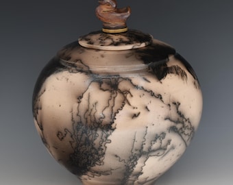 May include: A ceramic jar with a lid, featuring a duck-shaped handle. The jar has a round shape with a light beige base and black, lightning-like patterns. The lid is beige with black markings and a gold-colored band.