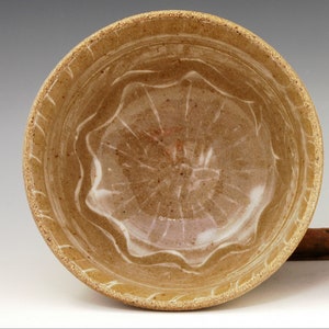 May include: Handmade ceramic bowl with a speckled, tan exterior and a wavy, white-lined interior. The bowl is approximately 3.1 inches high and 6.2 inches wide, perfect for serving or display.
