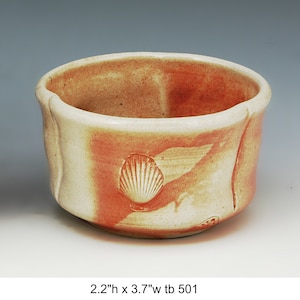 May include: A small, white ceramic bowl with a red glaze and a seashell design. The bowl is 2.2 inches tall and 3.7 inches wide.