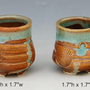 Puede incluir: Dos tazas de cerámica hechas a mano con un diseño de concha. Las tazas son marrones con un borde turquesa y miden 5,1 cm de alto por 4,3 cm de ancho y 4,3 cm de alto por 4,3 cm de ancho.