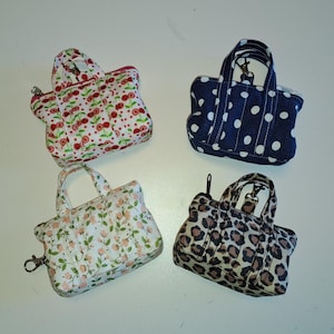 Pode incluir: Quatro pequenas bolsas de tecido em forma de mini sacolas, cada uma com duas alças e fecho de zíper. Os padrões incluem cerejas vermelhas sobre branco, bolinhas brancas sobre azul marinho, pequenas flores rosas sobre branco e estampa de leopardo.