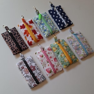 Peut inclure: Huit pochettes rectangulaires en tissu avec fermetures éclair et mousquetons en métal. Les pochettes présentent divers motifs dont léopard, feuilles d'automne, fleurs bleues, pois blancs, icônes médicales, fraises, tulipes jaunes et fleurs pastel.