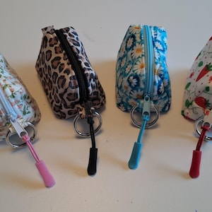 May include: Four small zipped pouches with key rings, each featuring a distinct pattern: a floral print, a leopard print, a blue daisy print, and a strawberry print. Each pouch has a matching coloured zip pull attached to a silver metal ring.