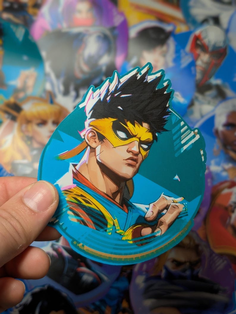 May include: A round sticker featuring a cartoon character with black hair, a yellow headband, and a blue and yellow outfit. The character is wearing a blue mask with a yellow stripe. The sticker has a blue background with a white outline.