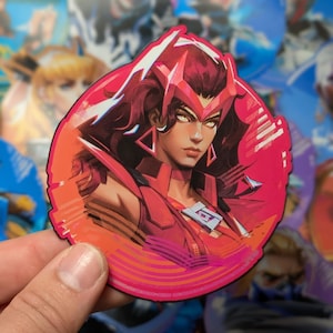 May include: A round sticker featuring a female character with red hair and a red and white costume. The character has a serious expression and is surrounded by a pink and white background with a geometric pattern.