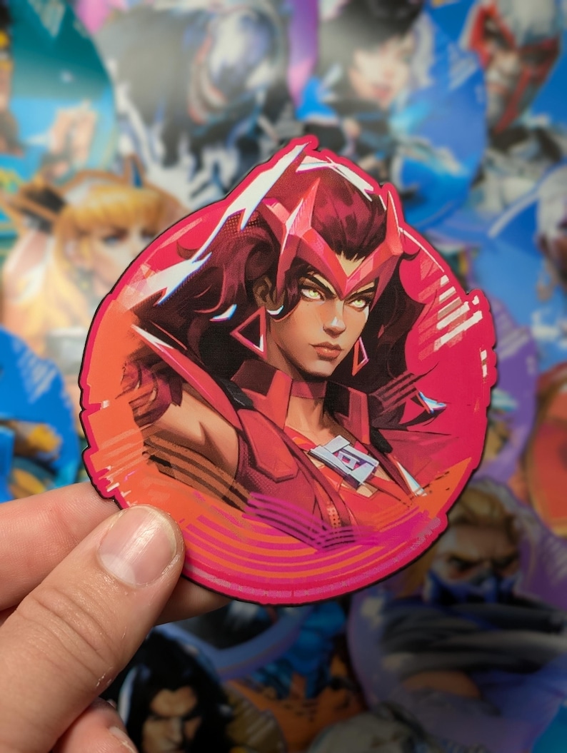 May include: A round sticker featuring a female character with red hair and a red and white costume. The character has a serious expression and is surrounded by a pink and white background with a geometric pattern.