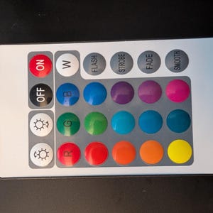 May include: A rectangular, silver remote control with various buttons. It features "ON", "OFF", "W", and colour options including blue, green, and red. Other buttons provide light control functions like "FLASH" and "SMOOTH".