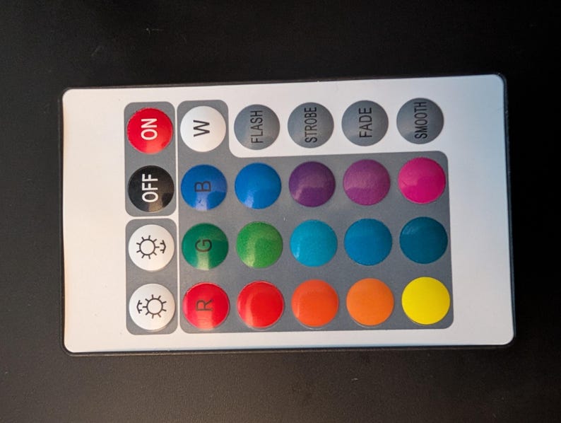 May include: A rectangular, silver remote control with various buttons. It features "ON", "OFF", "W", and colour options including blue, green, and red. Other buttons provide light control functions like "FLASH" and "SMOOTH".