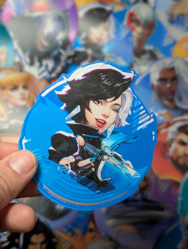 May include: A blue and white circular sticker featuring a cartoon illustration of a woman with black hair and blue eyes. She is wearing a black and white outfit and holding a weapon. The sticker has a white border and a blue background.