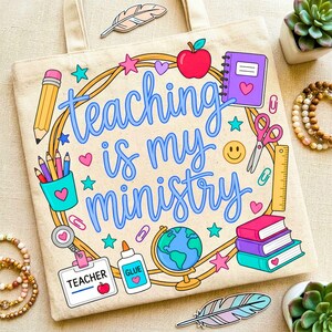 May include: Beige tote bag with the phrase "Teaching is my ministry" in blue script. The design includes a pencil, apple, notebook, globe, and other school-themed illustrations in bright colors. A perfect gift for teachers.