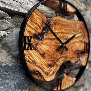 Puede incluir: Un reloj redondo de madera con números romanos y agujas de metal negro. La esfera del reloj está hecha de una rebanada de madera natural con un patrón de veta único.