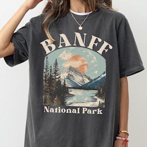 May include: A dark gray oversized t-shirt with a vintage-style graphic of a mountain landscape with a river and the text "Banff National Park".