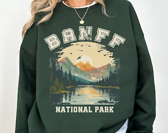 May include: Green sweatshirt with a vintage-style graphic of a mountain landscape and the text "BANFF NATIONAL PARK".