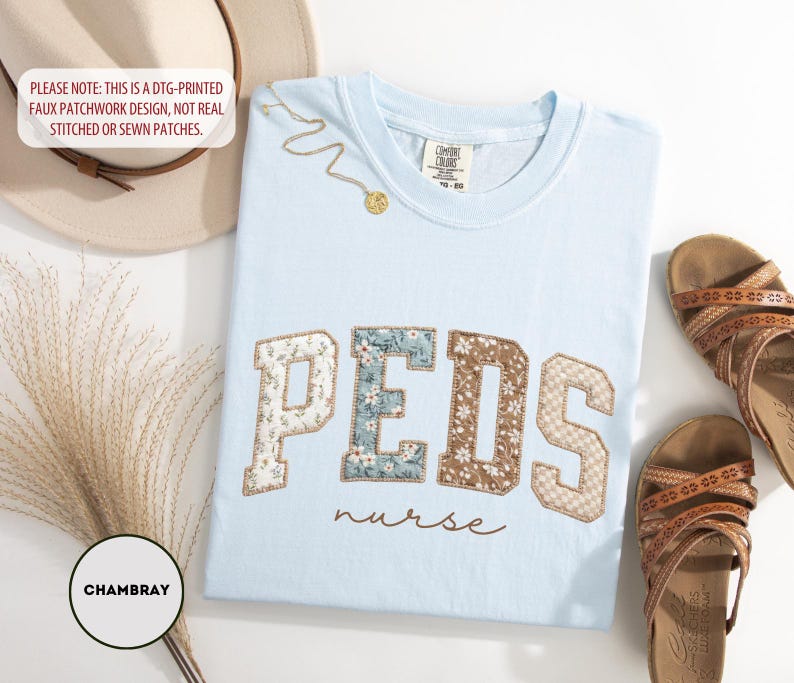 May include: Light blue t-shirt with "PEDS nurse" text. The word "PEDS" is in a patchwork design with floral and textured patterns. A gold necklace and brown sandals are also in the image. A hat and decorative plant are in the background.