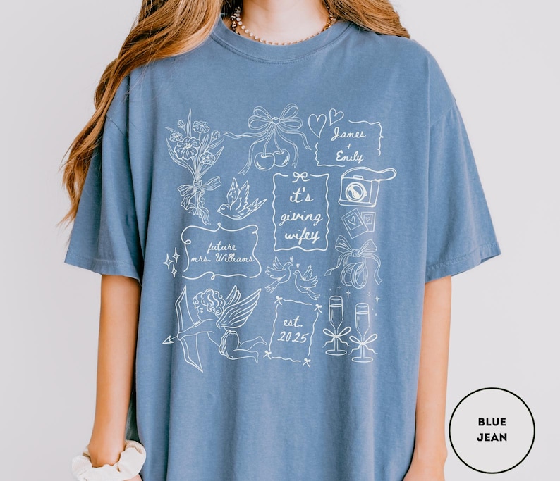 May include: A blue jean-colored t-shirt with white line art. The design includes flowers, bows, doves, a camera, champagne glasses, and the text "it's giving wifey", "future mrs. Williams", "James + Emily", and "est. 2025".