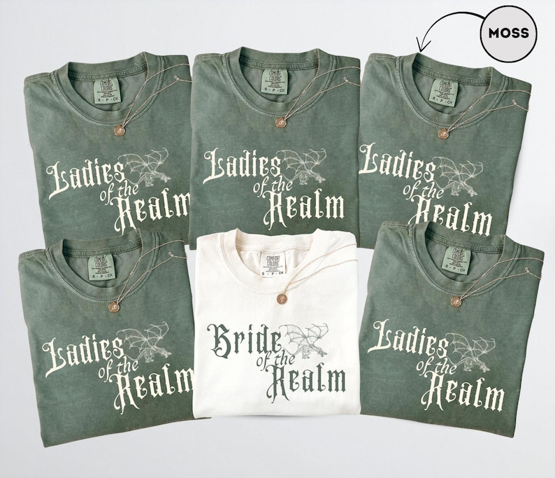 May include: Six t-shirts, five in moss green and one in cream. The green shirts read "Ladies of the Realm" in white script with a dragon graphic. The cream shirt says "Bride of the Realm". Each shirt has a gold necklace.