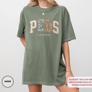 May include: Moss green t-shirt with "PEDS nurse" text in a faux patchwork design. The word "PEDS" is in a collegiate style font with floral and patterned patches. The shirt is a relaxed fit.