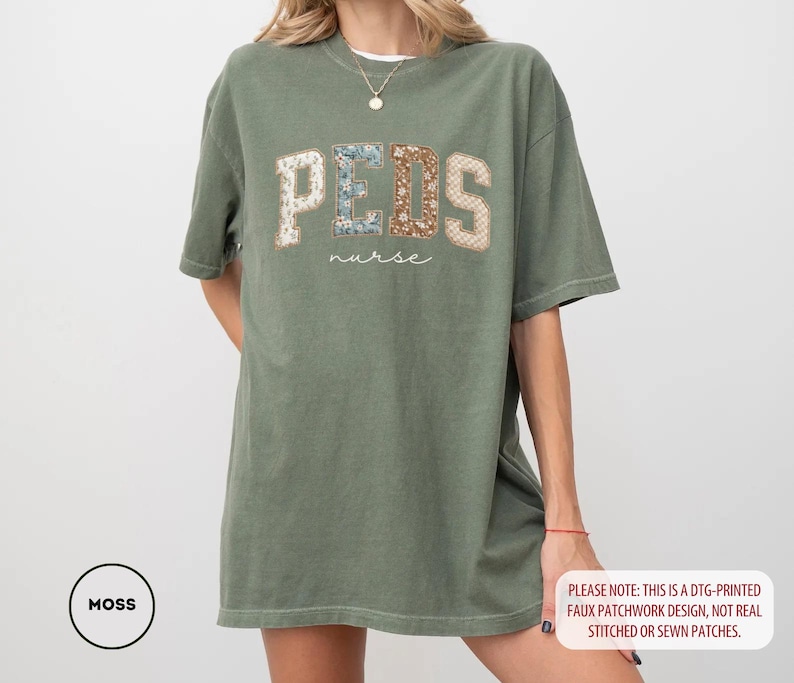 May include: Moss green t-shirt with "PEDS nurse" text in a faux patchwork design. The word "PEDS" is in a collegiate style font with floral and patterned patches. The shirt is a relaxed fit.
