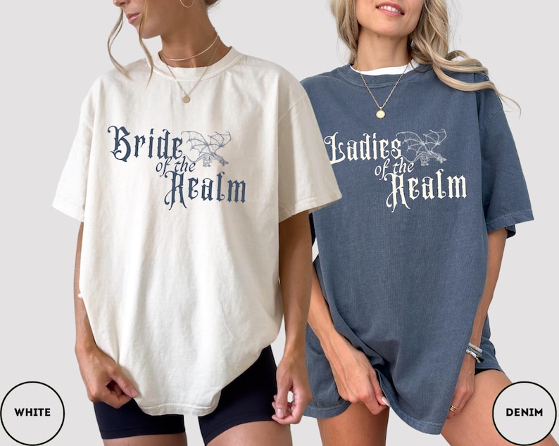 May include: Two short-sleeved t-shirts, one cream and one denim blue, featuring the text "Bride of the Realm" and "Ladies of the Realm" in a gothic font. Each shirt has a matching illustration of a dragon.