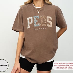 May include: Espresso-colored t-shirt with the word "PEDS" in a faux patchwork design, and the word "nurse" in a script font. The shirt has a relaxed fit and short sleeves. The text "PLEASE NOTE: THIS IS A DTG-PRINTED FAUX PATCHWORK DESIGN, NOT REAL STITCHED OR SEWN PATCHES." is also visible.