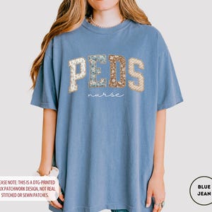 May include: A blue jean-colored t-shirt with the word "PEDS" in a faux patchwork design, with the word "nurse" below it. The letters have floral and patterned accents. The shirt is a comfortable, oversized fit.