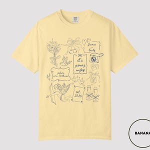 May include: A light yellow t-shirt with a navy blue graphic design. The design includes illustrations of flowers, bows, doves, a camera, champagne glasses, and text that reads "It's giving wifey", "future mrs. Williams", "James & Emily", and "est. 2025".