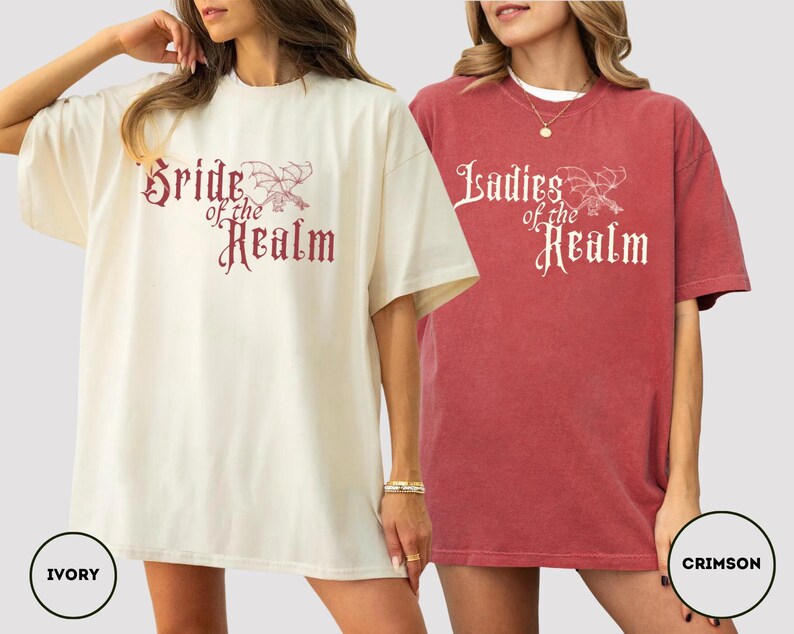 May include: Two oversized t-shirts, one ivory and one crimson, featuring the text "Bride of the Realm" and "Ladies of the Realm" in a decorative font. The shirts have short sleeves and a relaxed fit, perfect for casual wear.