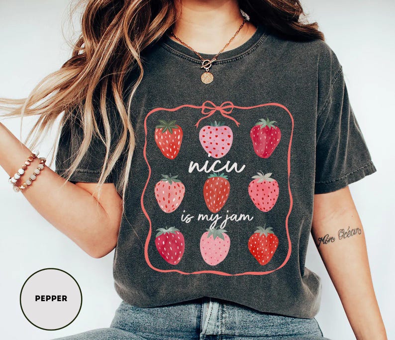 May include: Dark grey t-shirt featuring a pink framed design with nine strawberries in varying shades of red and pink. The text "NICU is my jam" is in the center. The shirt is a casual style.
