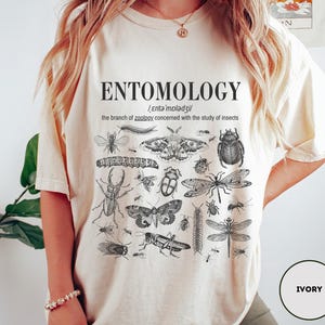 May include: A white t-shirt with the word "ENTOMOLOGY" printed in black. The shirt also features a definition of the word and a variety of insect illustrations.