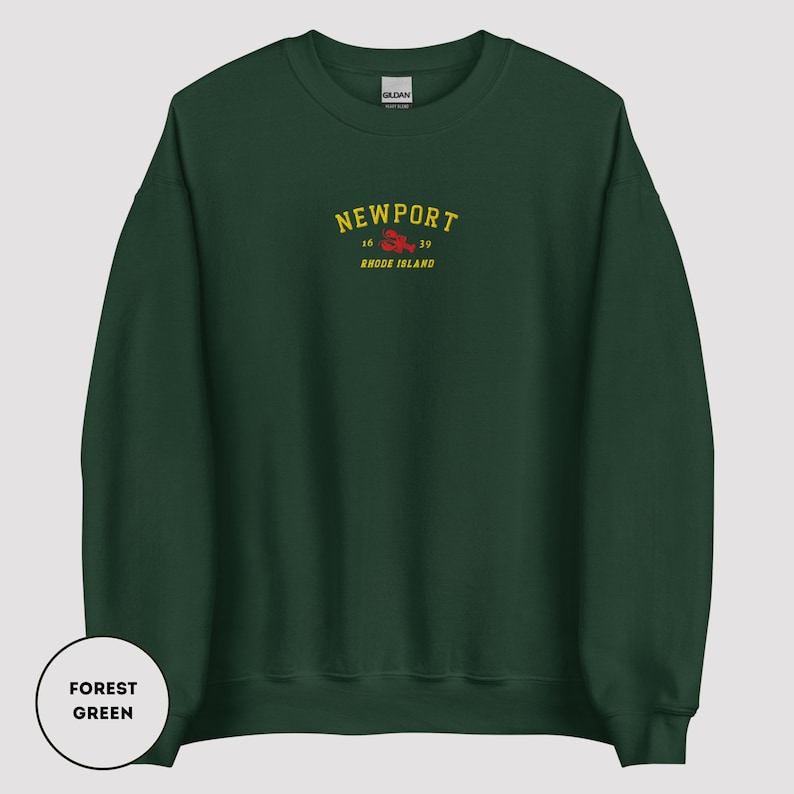 May include: Forest green sweatshirt featuring the word "NEWPORT" in yellow arched text, with "16 39" and "RHODE ISLAND" in smaller text. A red lobster graphic is below the text. The sweatshirt is a Gildan brand.