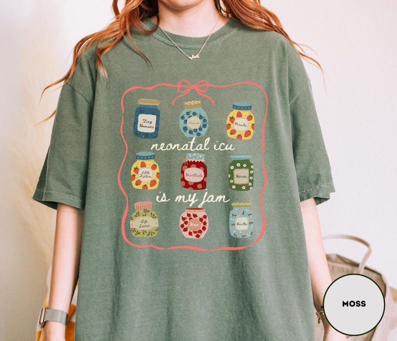 May include: Moss green t-shirt featuring a graphic of nine jam jars with different fruit designs. The text "neonatal icu is my jam" is written in a pink frame. The shirt is made of a soft material.