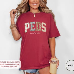 May include: A maroon t-shirt with the word "PEDS" in a faux patchwork design, with the word "nurse" below it. The shirt is a relaxed fit and has short sleeves. The text "PLEASE NOTE: THIS IS A DTG-PRINTED FAUX PATCHWORK DESIGN, NOT REAL STITCHED OR SEWN PATCHES." is at the bottom.