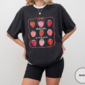 May include: Black t-shirt with a strawberry graphic and the text "NICU is my jam". The design features nine strawberries in various shades of red and pink, framed by a pink border and a bow.